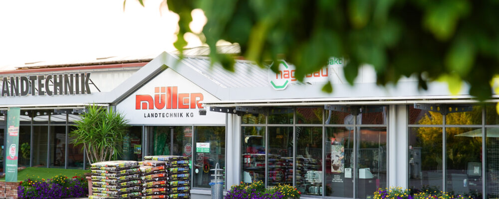 Eingang Müller Landtechnik Baumarkt in Holzhausen im Sonnenuntergang, vor dem Eingang stehen Paletten mit Blumenerde